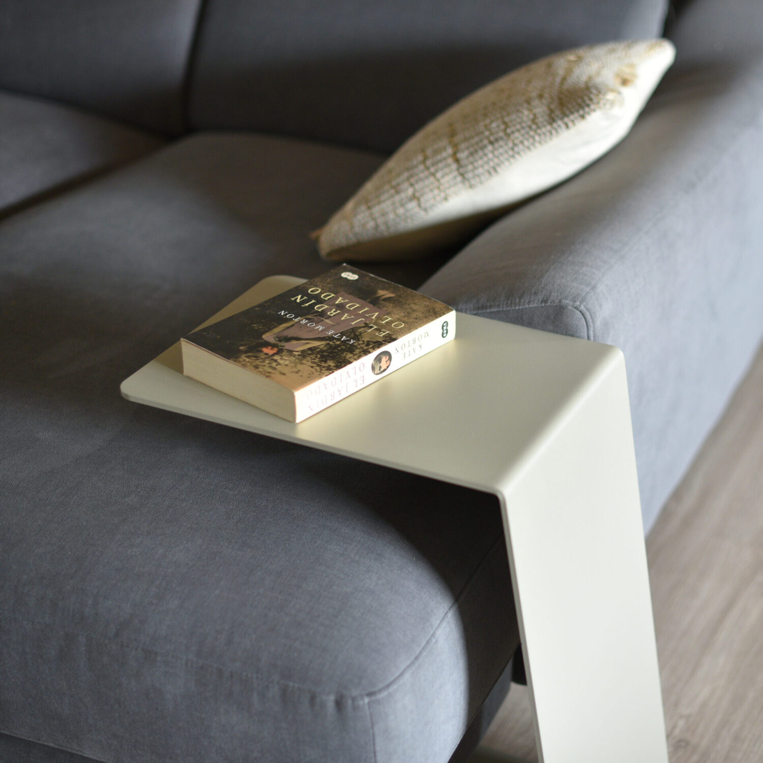 Detalle de la mesa auxiliar Armony Taupe colocada junto al sofá y con un libro sobre ella.